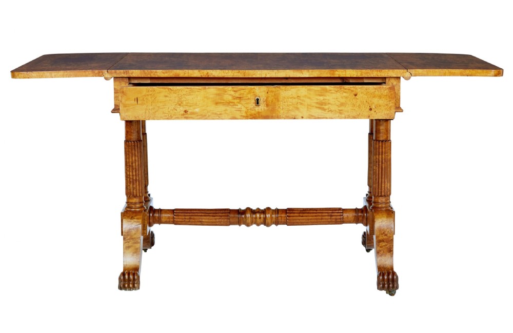 A nineteenth-century Biedermeier burr birch sofa table featuring twin drop leaves, a frieze drawer, fluted column supports, a turned central stretcher, and carved paw feet on castors. View IV