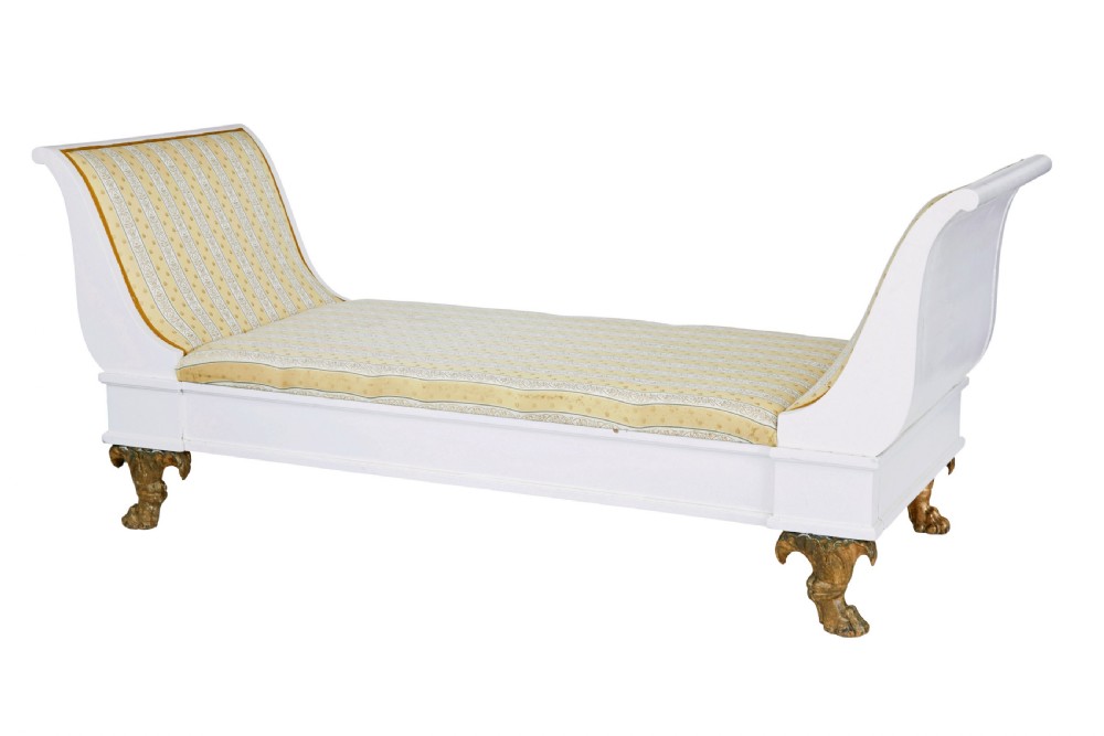 An early 20th-century Scandinavian Empire Revival day bed featuring a white painted frame, flared scroll ends, carved gilded paw feet, and yellow striped fabric upholstery.