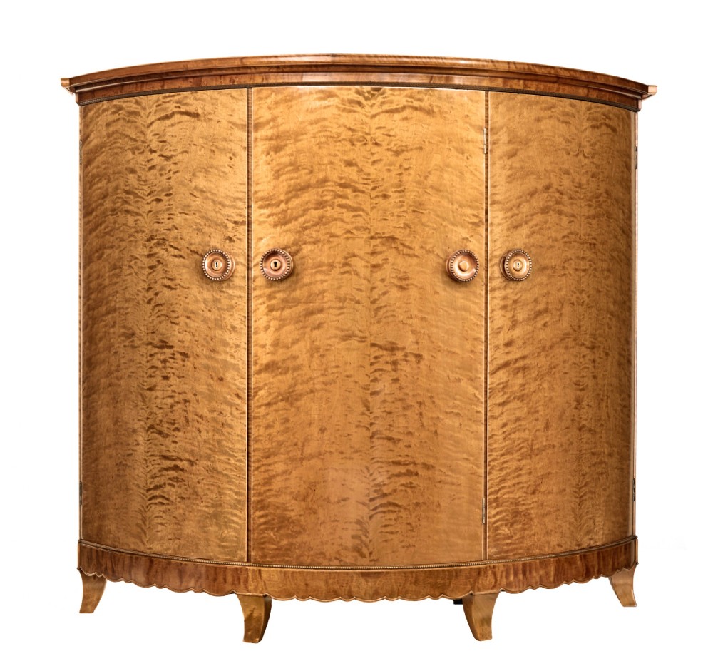 A large curved cabinet crafted from honey-coloured flame birch with four panelled doors, circular beaded keyholes, and a scalloped lower trim.