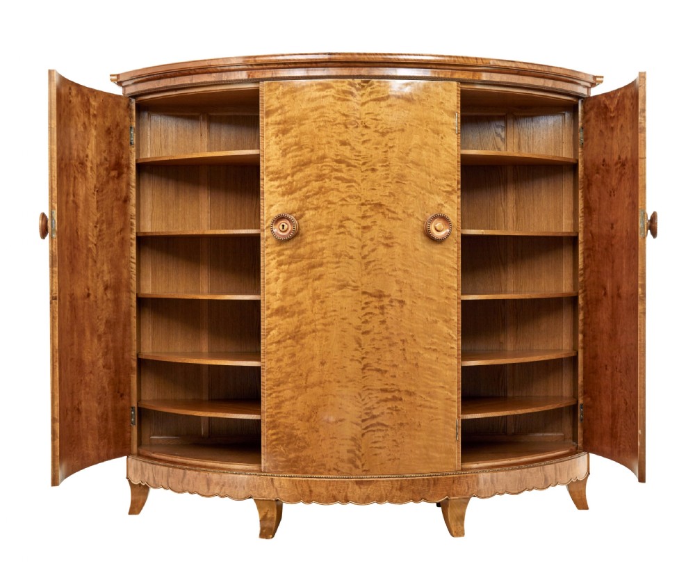 A large curved cabinet crafted from honey-coloured flame birch with four panelled doors, circular beaded keyholes, and a scalloped lower trim. View II