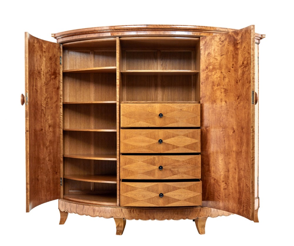A large curved cabinet crafted from honey-coloured flame birch with four panelled doors, circular beaded keyholes, and a scalloped lower trim. View IV