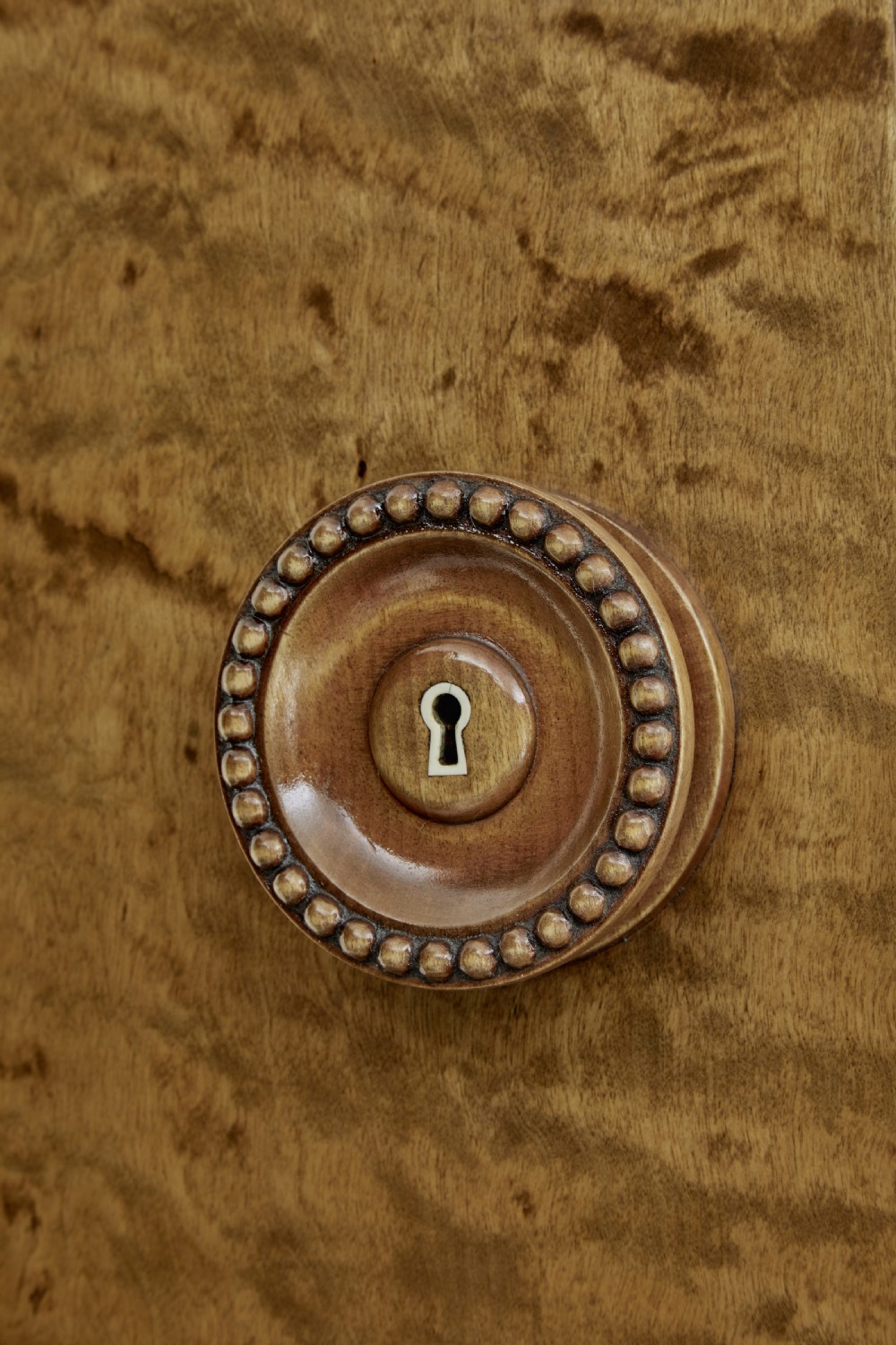 A large curved cabinet crafted from honey-coloured flame birch with four panelled doors, circular beaded keyholes, and a scalloped lower trim. View IX