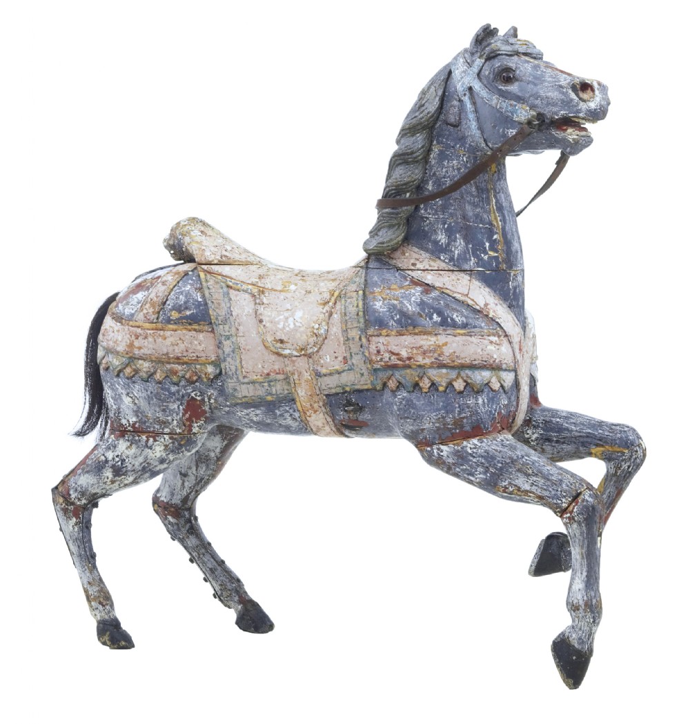 A carved wooden carousel horse sculpture with distressed blue and cream paint, detailed saddle, leather reins, and a raised front leg.