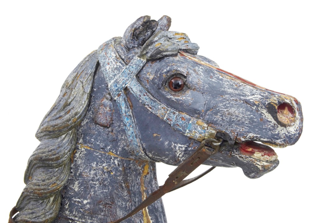 A carved wooden carousel horse sculpture with distressed blue and cream paint, detailed saddle, leather reins, and a raised front leg. View VIII