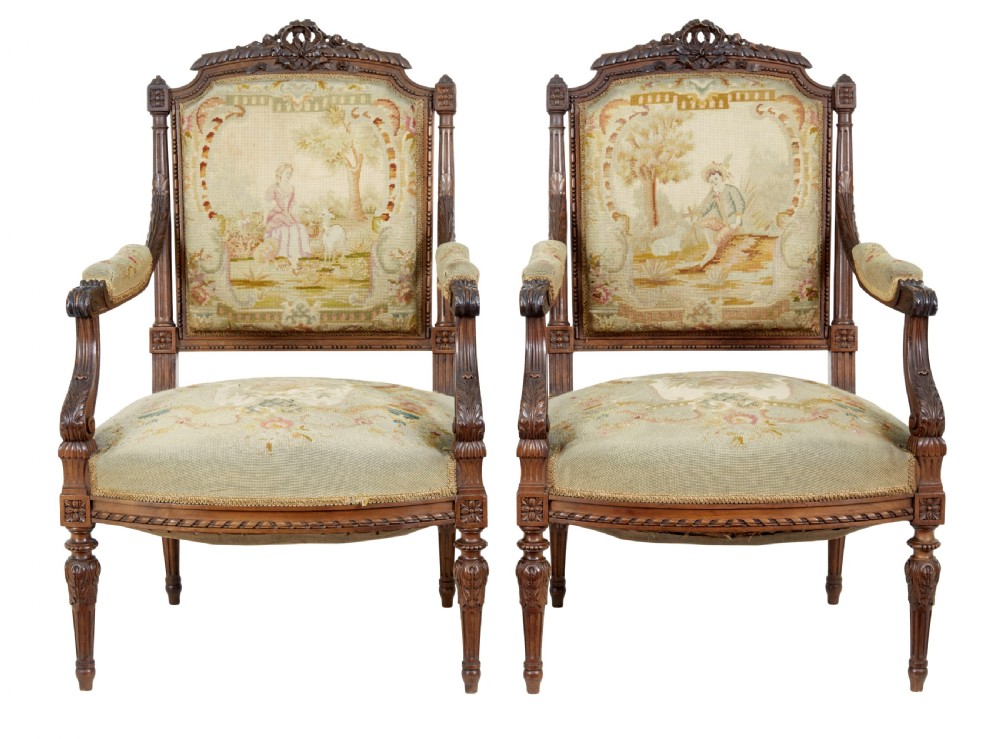 A pair of 19th-century French carved walnut armchairs upholstered in woven tapestry fabric featuring pastoral scenes and fluted turned legs.