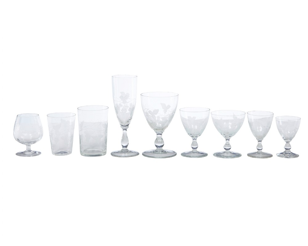 A nine-piece collection of clear 1930s glass stemware and tumblers with etched vine patterns arranged in a line.