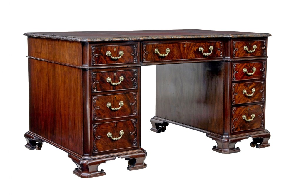An early 20th-century mahogany pedestal desk featuring nine carved drawers with brass handles, a leather inset top, and bracket feet.