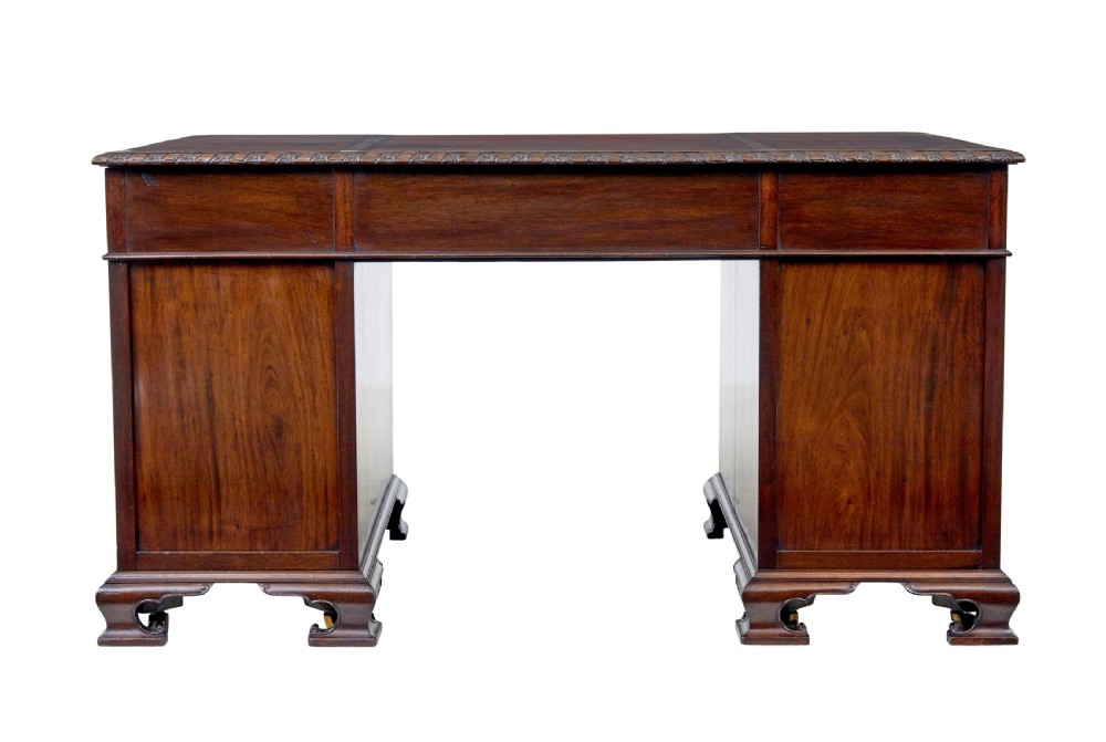 An early 20th-century mahogany pedestal desk featuring nine carved drawers with brass handles, a leather inset top, and bracket feet. View V