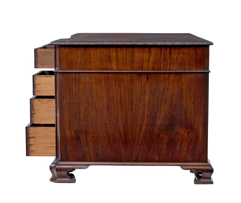 An early 20th-century mahogany pedestal desk featuring nine carved drawers with brass handles, a leather inset top, and bracket feet. View VI