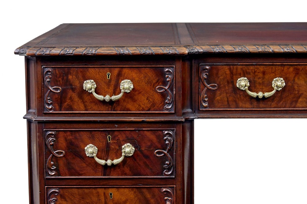 An early 20th-century mahogany pedestal desk featuring nine carved drawers with brass handles, a leather inset top, and bracket feet. View IX