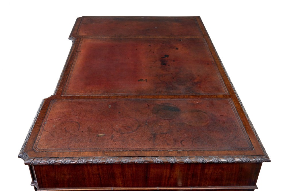 An early 20th-century mahogany pedestal desk featuring nine carved drawers with brass handles, a leather inset top, and bracket feet. View X