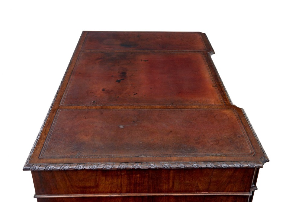 An early 20th-century mahogany pedestal desk featuring nine carved drawers with brass handles, a leather inset top, and bracket feet. View XI
