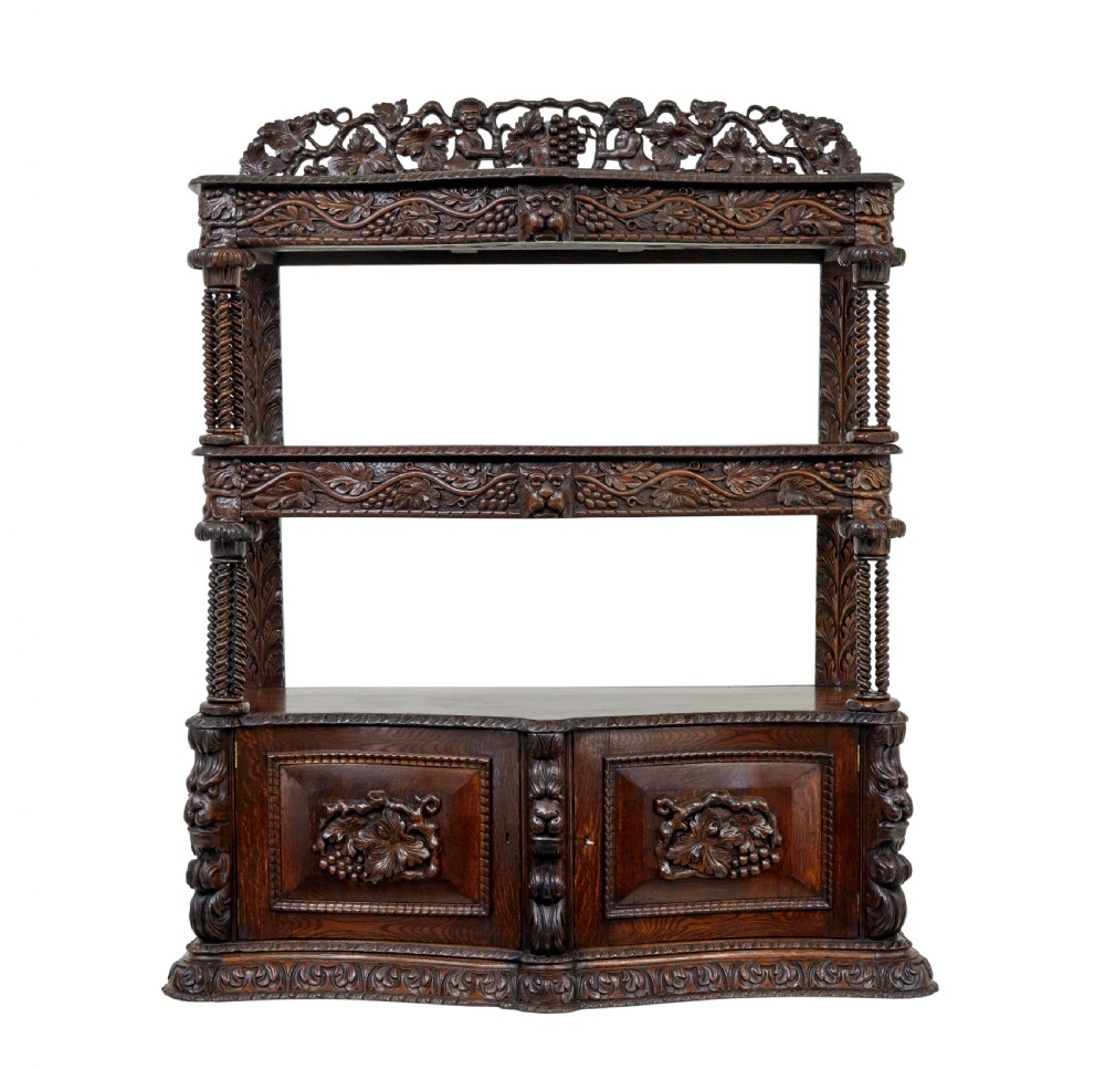 A 19th-century dark oak Victorian buffet featuring three tiers, intricate grapevine relief carvings, turned support columns, and a lower double-door cupboard.