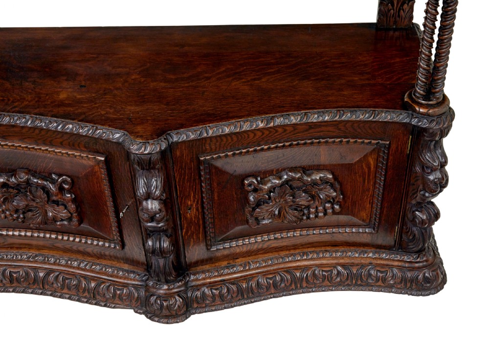 A 19th-century dark oak Victorian buffet featuring three tiers, intricate grapevine relief carvings, turned support columns, and a lower double-door cupboard. View III