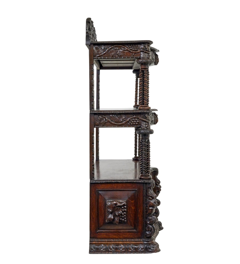 A 19th-century dark oak Victorian buffet featuring three tiers, intricate grapevine relief carvings, turned support columns, and a lower double-door cupboard. View VI