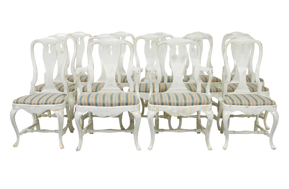 A set of fourteen distressed off-white lacquered Queen Anne style dining chairs featuring vasiform splats, cabriole legs, and striped textile upholstery.