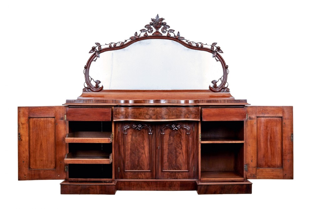 A Victorian flame mahogany sideboard featuring a carved botanical frame around an oval mirror top above cupboard doors and pedestal bases. View II