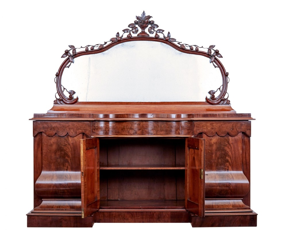 A Victorian flame mahogany sideboard featuring a carved botanical frame around an oval mirror top above cupboard doors and pedestal bases. View III