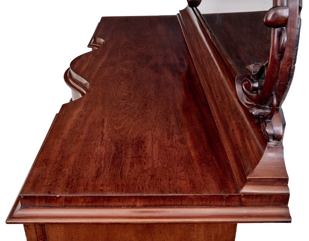 A Victorian flame mahogany sideboard featuring a carved botanical frame around an oval mirror top above cupboard doors and pedestal bases. View V