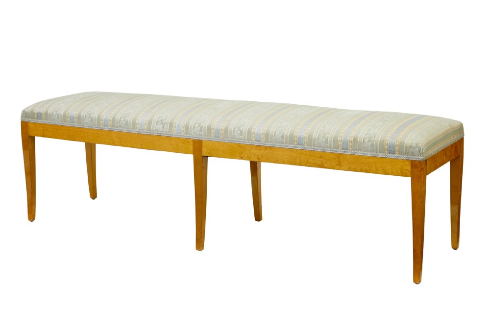 An early 20th-century Swedish long stool made of light honey-coloured birch wood with six square tapered legs and light blue striped upholstered seat.