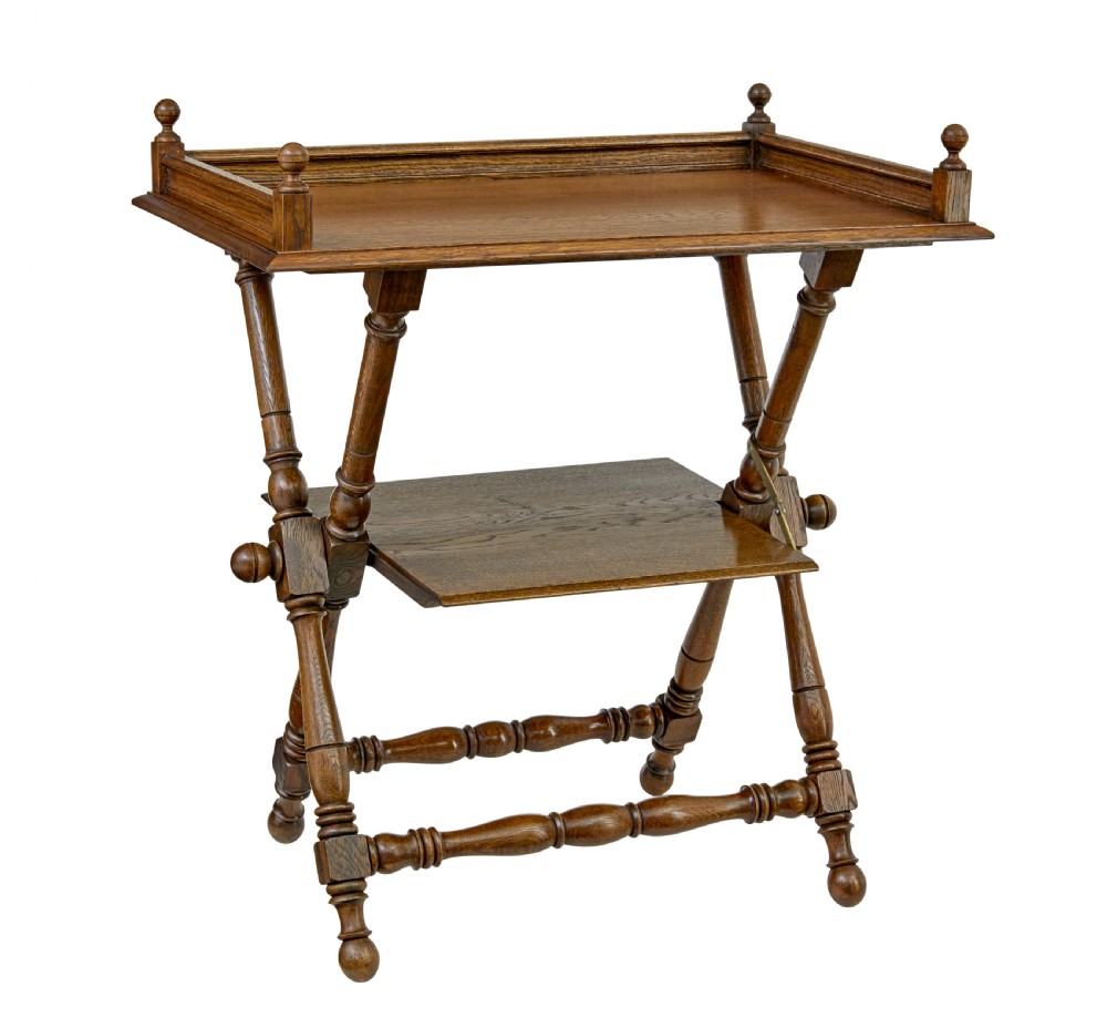 A 19th-century oak butlers tray table featuring a gallery-edged top tray with corner finials, a lower tiered shelf, and turned X-frame folding legs.
