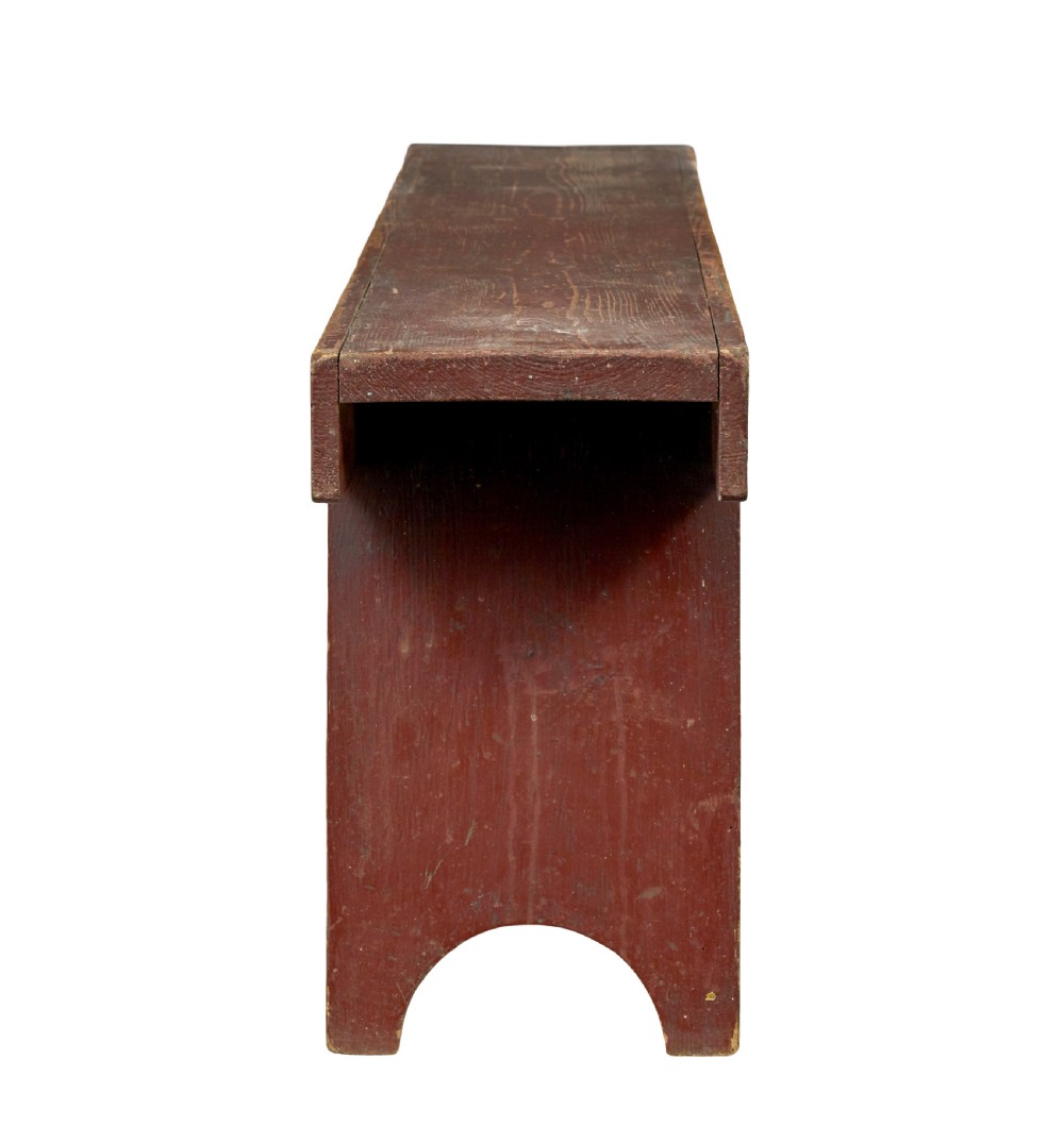 A long 19th-century Swedish pine bench painted in a distressed red finish with slab trestle legs featuring arched cut-outs. View V