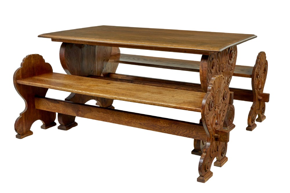 A 19th-century carved oak dining table flanked by two matching wooden benches with relief carvings on the trestle end supports.
