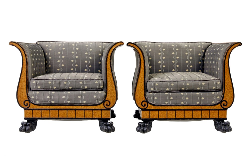 A pair of Art Deco armchairs featuring flared burr birch frames, grey upholstered cushions with a pattern motif, and ebonised carved feet.