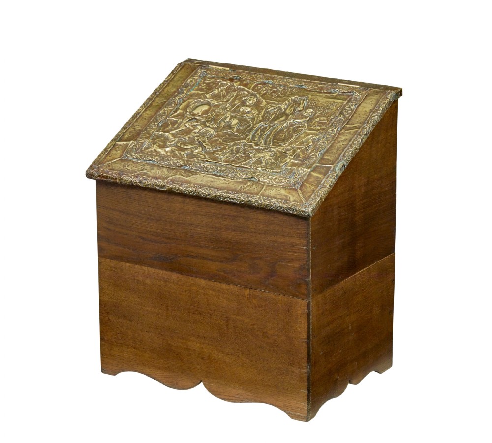 A 19th-century oak sloped-top storage box featuring an embossed brass lid panel depicting figures on horseback and a scalloped wooden base.