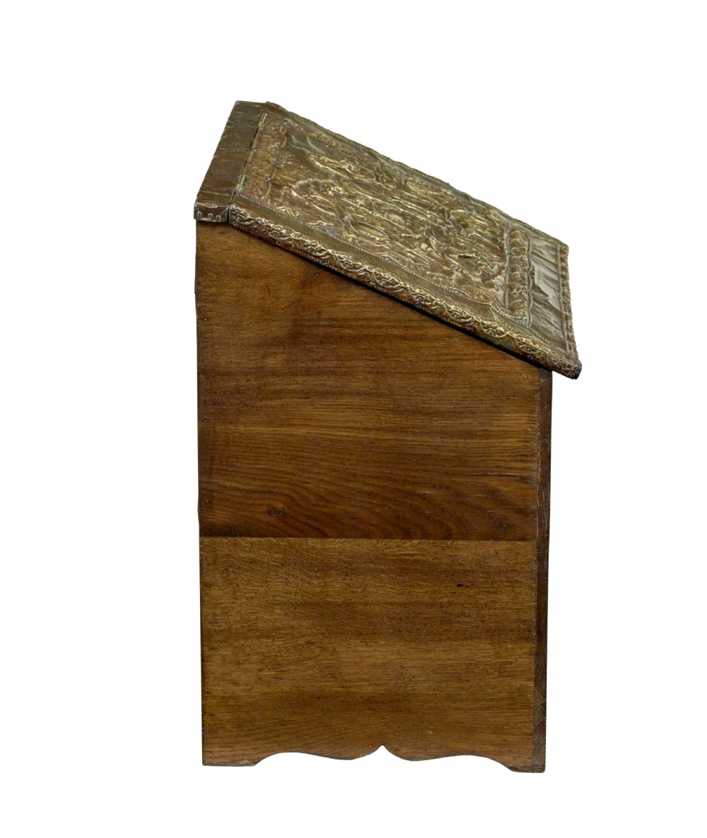 A 19th-century oak sloped-top storage box featuring an embossed brass lid panel depicting figures on horseback and a scalloped wooden base. View VI
