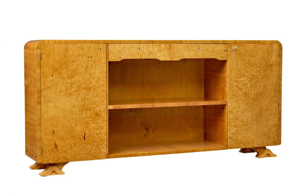 A low Scandinavian Art Deco open bookcase in golden burr elm with rounded upper corners, flanked cupboards, open central shelves, and sculpted feet.