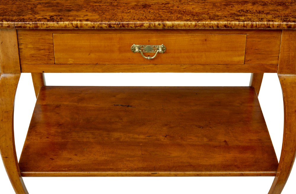 A 19th-century fruitwood and alder occasional table featuring curved legs, a single drawer with a brass handle, a lower shelf, and a figured wood top. View V