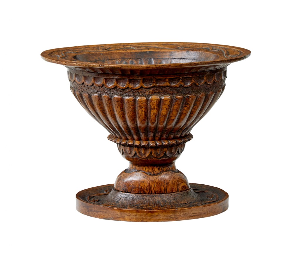 A 19th-century carved oak pedestal bowl featuring deep fluted sides, carved scrollwork along the rim, and a turned circular base.