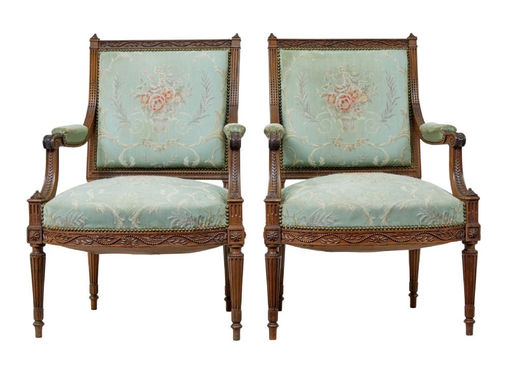 A pair of 19th-century French carved walnut armchairs featuring sage green floral tapestry upholstery, fluted legs, and padded armrests.