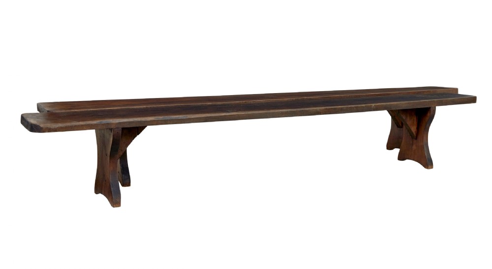 A pair of long early twentieth-century dark pine wooden benches with trestle-style legs.