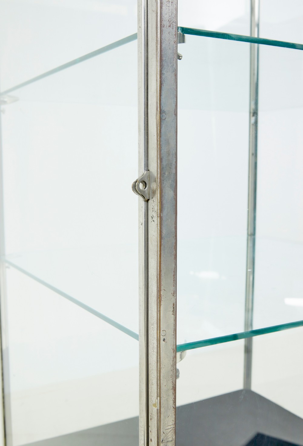 A tall rectangular Art Deco display cabinet featuring transparent glass sides and glass shelves within a thin steel frame, set upon a black leather-clad base with short brass-tipped legs. View V