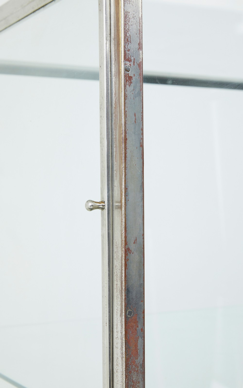 A tall rectangular Art Deco display cabinet featuring transparent glass sides and glass shelves within a thin steel frame, set upon a black leather-clad base with short brass-tipped legs. View VI