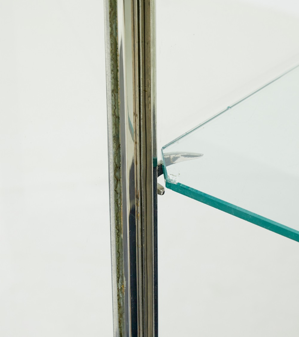 A tall rectangular Art Deco display cabinet featuring transparent glass sides and glass shelves within a thin steel frame, set upon a black leather-clad base with short brass-tipped legs. View VIII