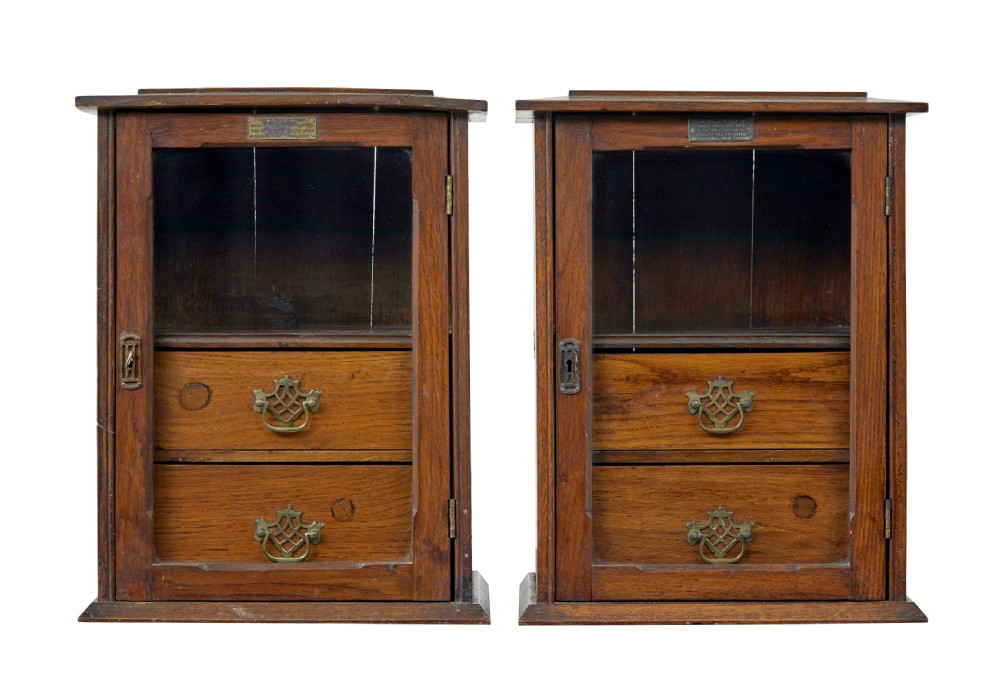 A pair of antique warm brown oak tabletop cabinets featuring glazed doors, brass keyhole escutcheons, and two internal drawers with decorative brass handles.