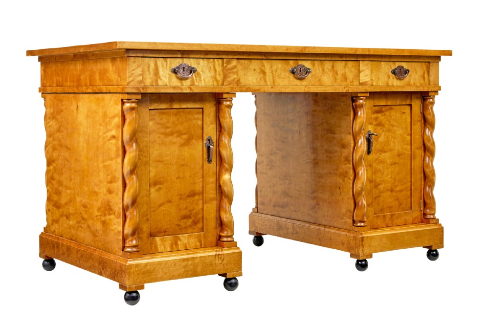A Swedish early 20th-century pedestal desk crafted from golden flame birch wood featuring barley twist corner columns and spherical black feet.