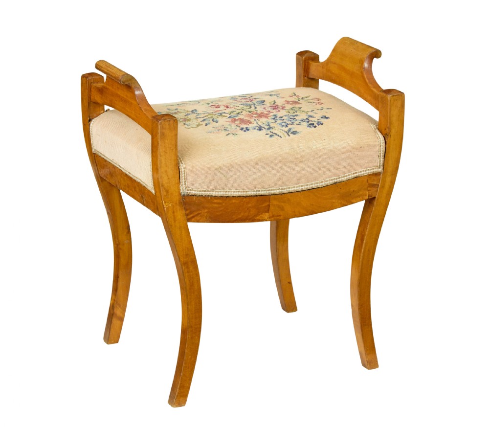A mid-19th-century Swedish birch Empire stool featuring curved sabre legs, side handles, and a needlepoint upholstered seat with floral embroidery.