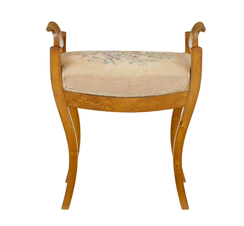 A mid-19th-century Swedish birch Empire stool featuring curved sabre legs, side handles, and a needlepoint upholstered seat with floral embroidery. View IV