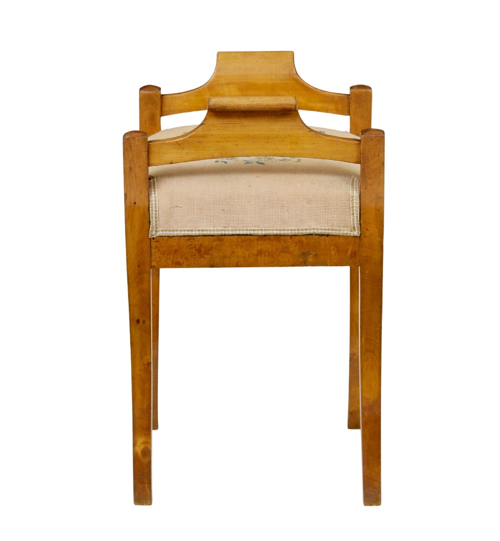 A mid-19th-century Swedish birch Empire stool featuring curved sabre legs, side handles, and a needlepoint upholstered seat with floral embroidery. View V