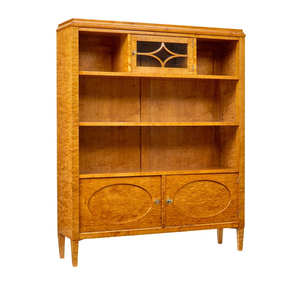 An early 20th-century Swedish Grace satin birch open bookcase featuring a small glazed upper door, open shelving, and a double-door lower cabinet with oval panelling.