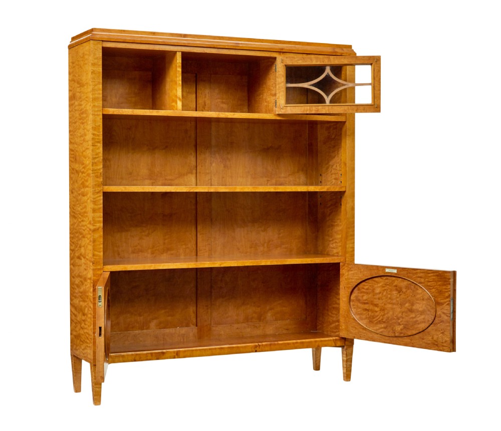 An early 20th-century Swedish Grace satin birch open bookcase featuring a small glazed upper door, open shelving, and a double-door lower cabinet with oval panelling. View II
