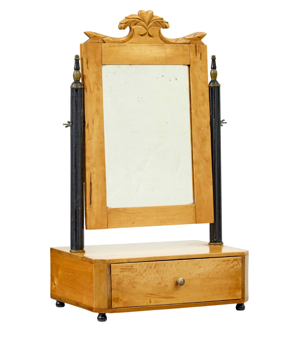 A 19th-century Swedish light birch tabletop vanity mirror featuring a carved top crest, ebonised side columns with brass finials, and a base drawer on bun feet.