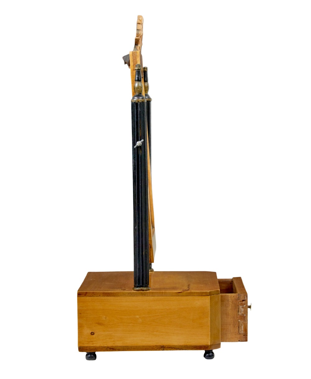 A 19th-century Swedish light birch tabletop vanity mirror featuring a carved top crest, ebonised side columns with brass finials, and a base drawer on bun feet. View II