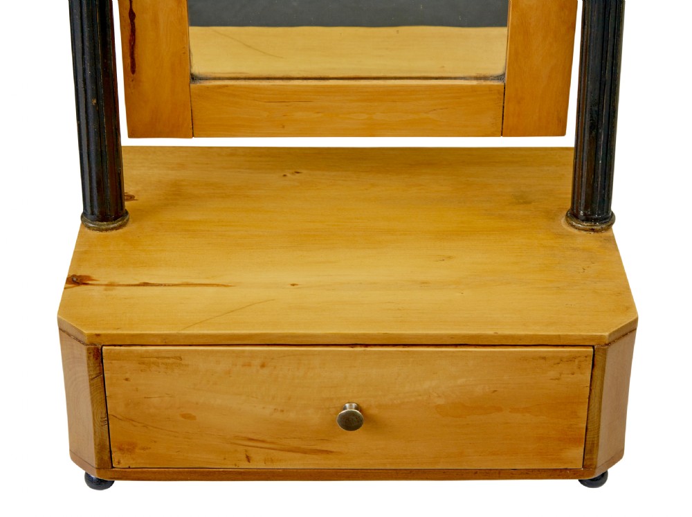 A 19th-century Swedish light birch tabletop vanity mirror featuring a carved top crest, ebonised side columns with brass finials, and a base drawer on bun feet. View V