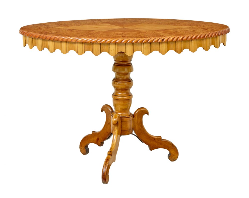A nineteenth-century oval occasional table crafted from inlaid burr birch with a scalloped apron, turned central pedestal, and four carved scrolled legs.
