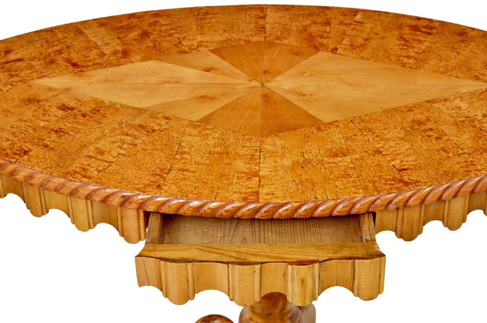A nineteenth-century oval occasional table crafted from inlaid burr birch with a scalloped apron, turned central pedestal, and four carved scrolled legs. View V